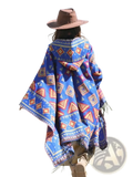 A vibrant blue knitted hooded poncho cape with red orange and white geometric patterns and fringed edges