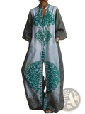 A long flowing light gray kaftan dress with bold teal geometric and floral embroidery on the front