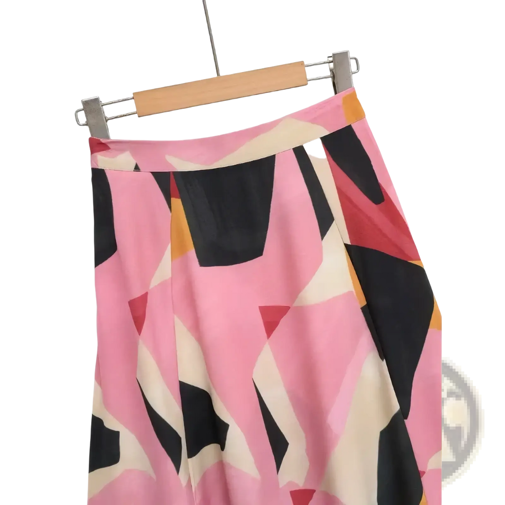 Geometric satin midi skirt in pink black and cream with an abstract geometric print hanging on a wooden hanger