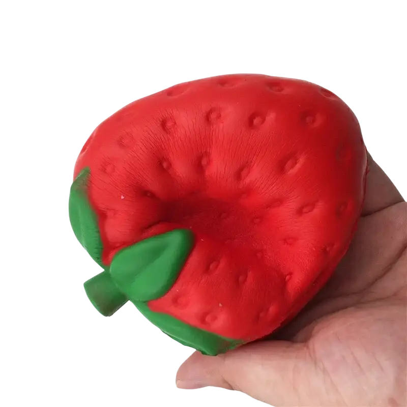 A vibrant red strawberry-shaped slow rising squishy stress relief ball with green leafy top and textured surface