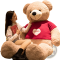 A plush tan giant teddy bear wearing a red knitted sweater with a white heart patch reading loves