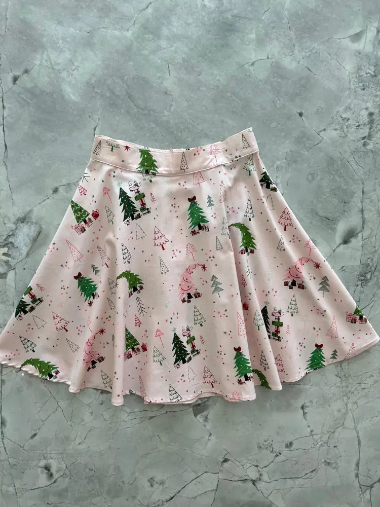 A light pink cotton skater skirt with a flared design and festive pine trees snowmen and house patterns