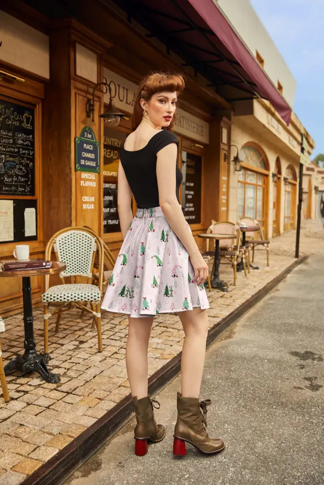 A woman wears a festive pink holiday gifts cotton skater skirt with green pine trees and red ornaments pattern