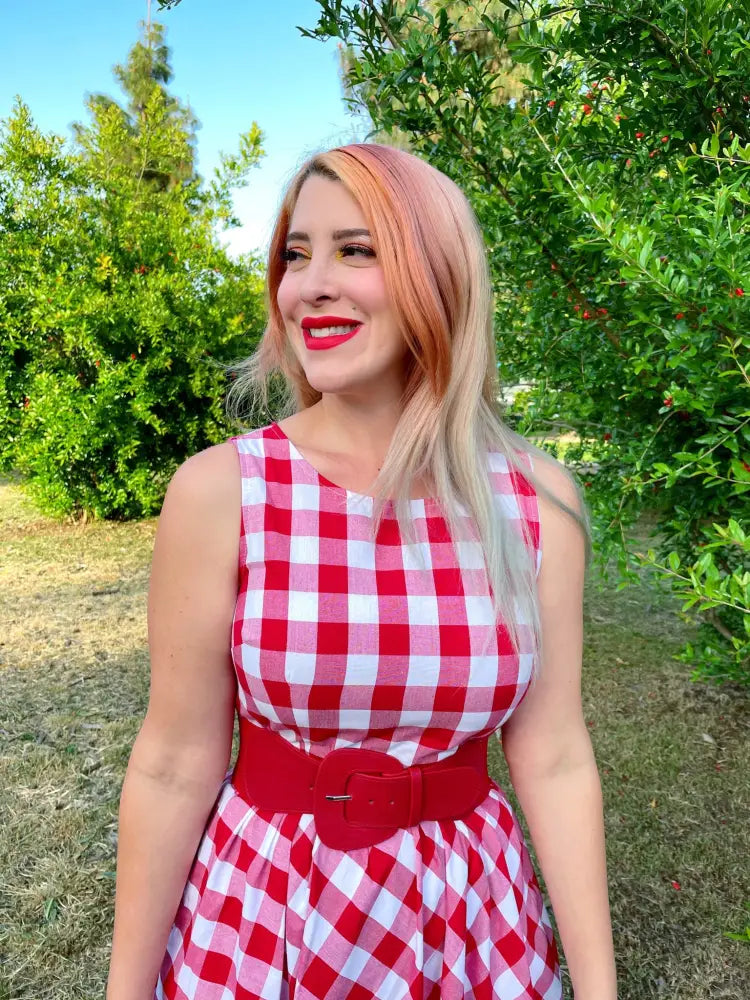 A woman wears a red and white gingham 1950s vintage cotton midi swing dress with a matching wide belt