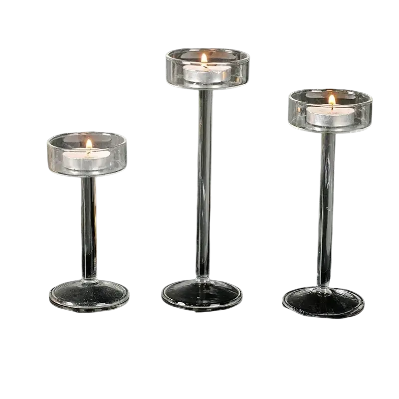 Three clear glass pillar candle holders with slender stems and lit tea lights for modern table decor