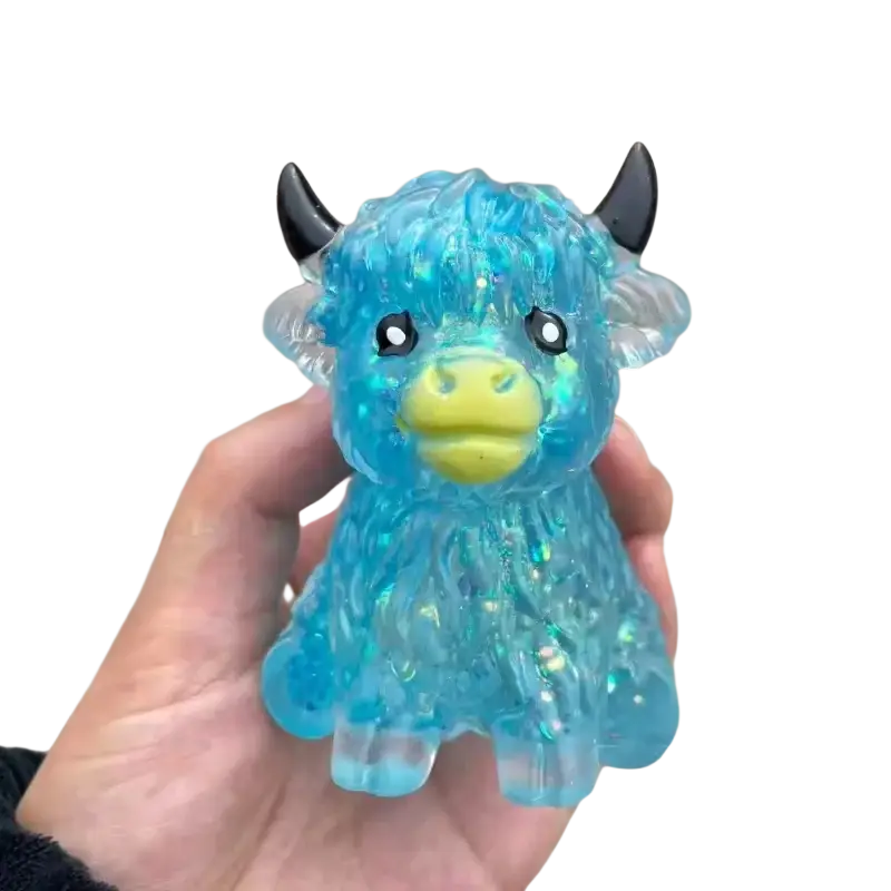 Translucent blue glitter highland cow slow rising squishy toy with black horns and yellow snout made of plastic