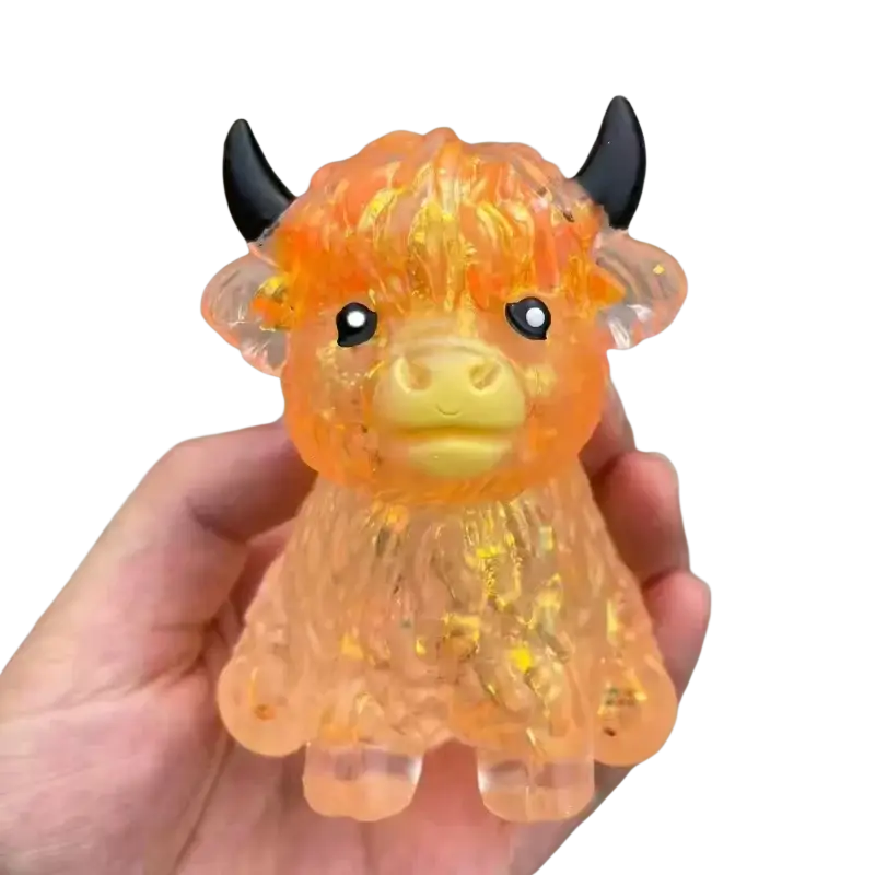 A translucent orange and yellow glittery plastic highland cow slow rising squishy toy with black horns