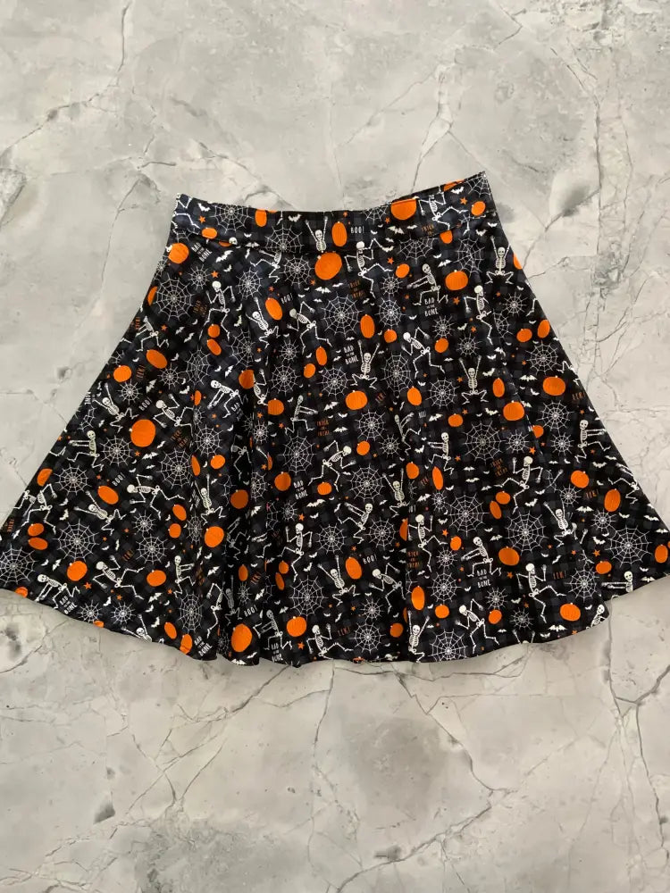 Black pleated skater skirt with glow in the dark orange pumpkins white skeletons and spiderwebs halloween pattern