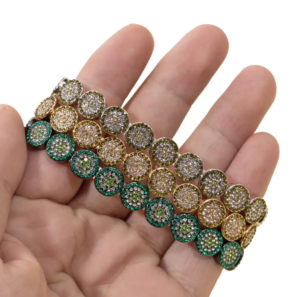 A hand holds two stacked gold color zinc alloy bangle style crystal bracelets with circular green and clear gemstones