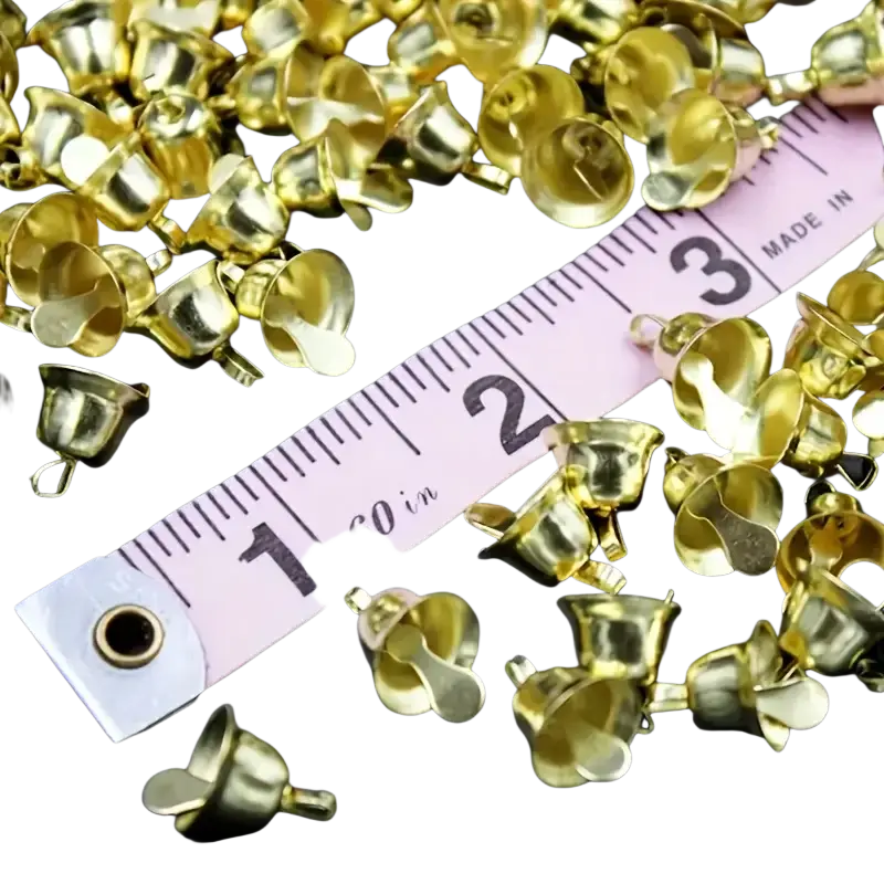 Gold metal sleigh bells 20 pcs scattered around a pink measuring tape showcasing bell-shaped metal charms