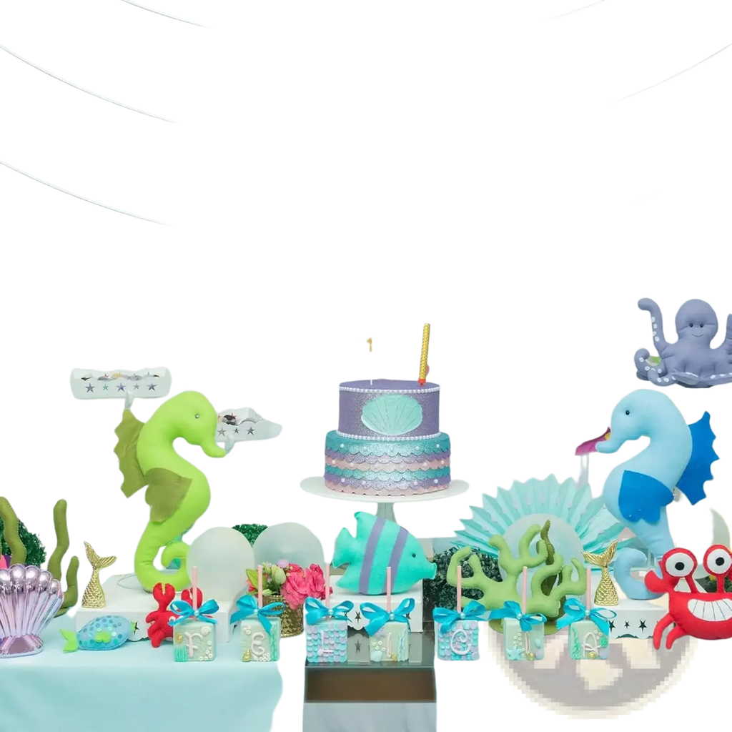 Two-tiered birthday cake with purple and teal mermaid-scale design topped with seashell centerpiece and candle for gold sea animal first birthday banner undersea decor