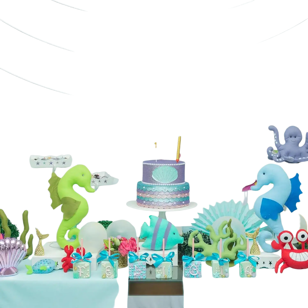 Two-tiered birthday cake with purple and teal mermaid-scale design topped with seashell centerpiece and candle for gold sea animal first birthday banner undersea decor