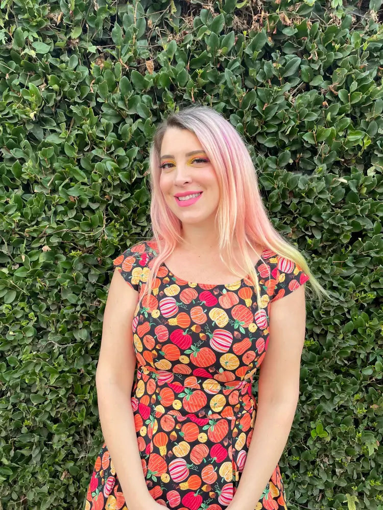 A woman wears a black cotton a-line dress with colorful vintage cartoonish pumpkin print gourdgeous margaret