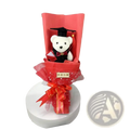 A plush white teddy bear wearing a black graduation cap and red bow tie in a red bouquet with glitter accents