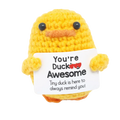 A yellow crocheted duck with black bead eyes and orange beak holding a white sign saying youre ducking awesome graduation gift 2025