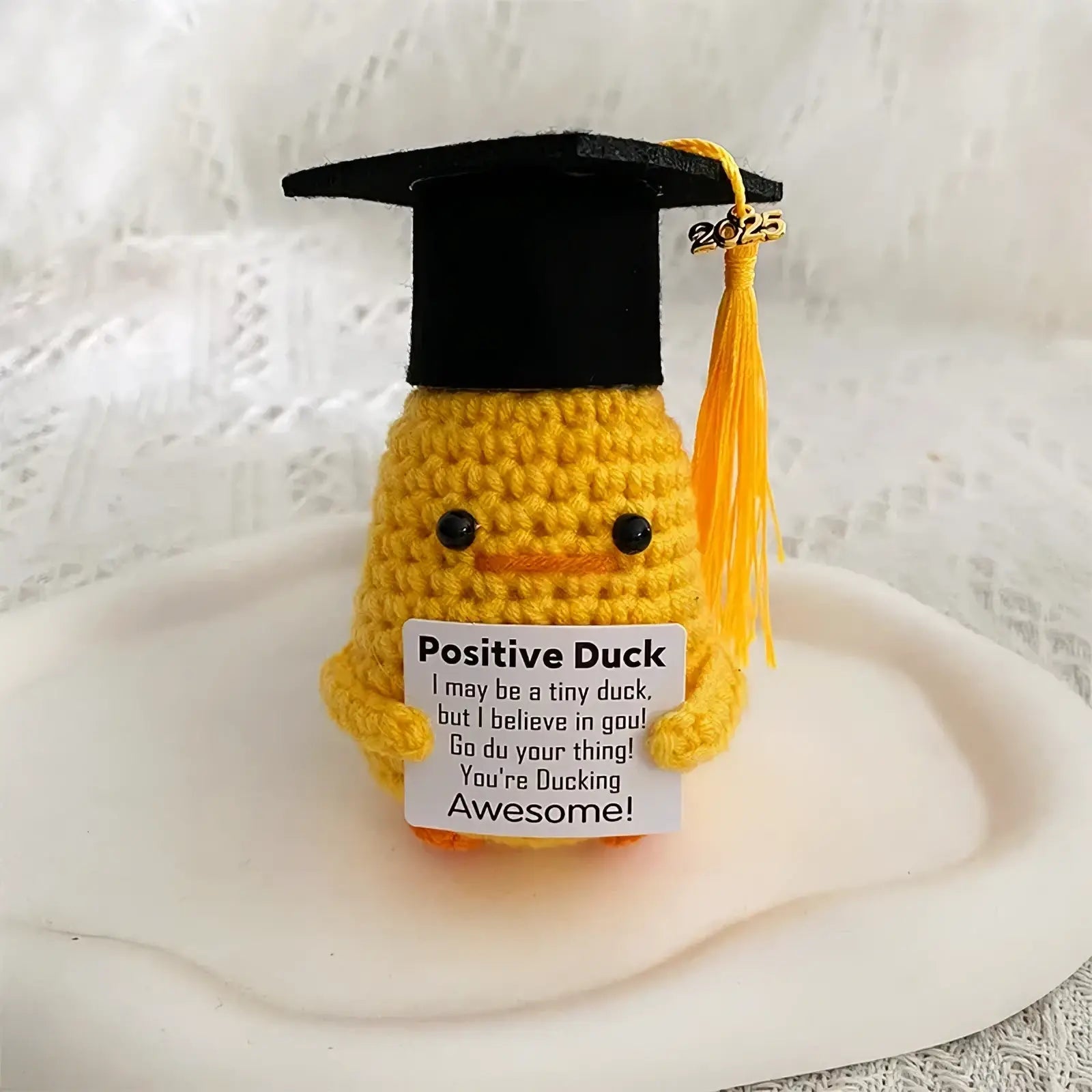 Yellow crocheted duck wearing black graduation cap with gold tassel holding white positive duck sign graduation gift