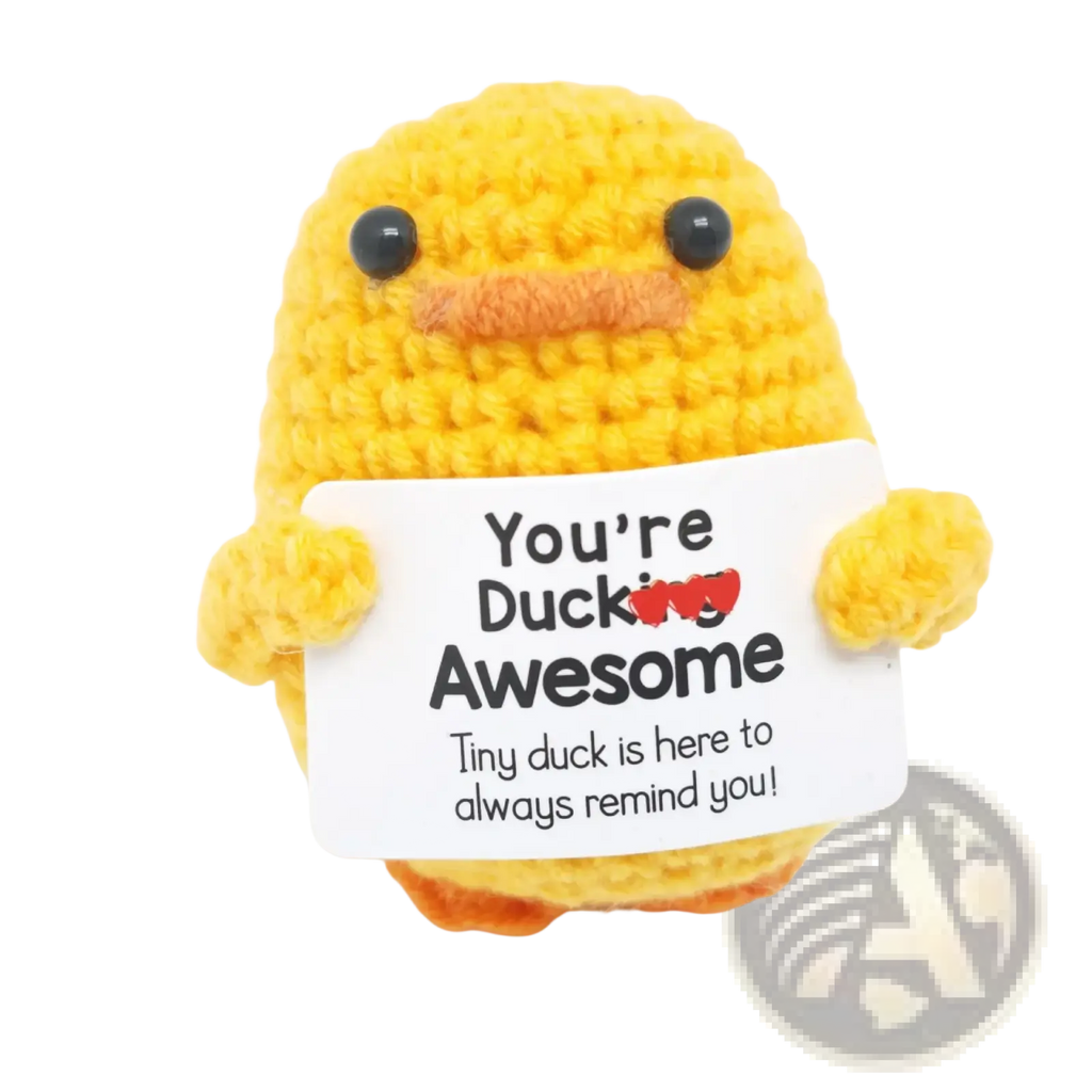 A yellow crocheted duck with black bead eyes and orange beak holding a white sign saying youre ducking awesome graduation gift 2025