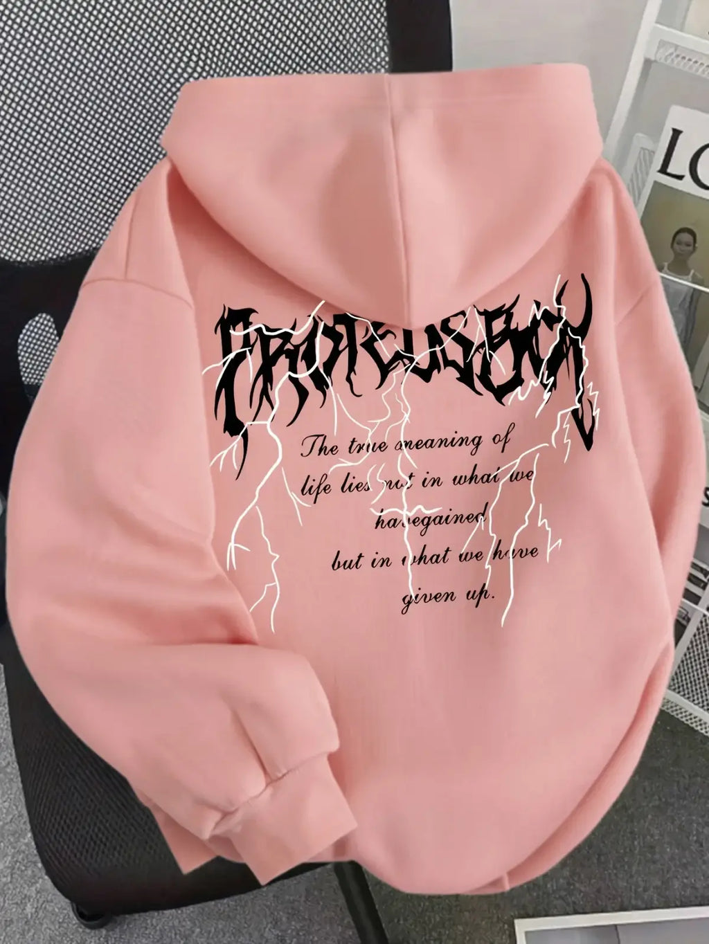 The back side of a soft pink graphic hooded sweatshirt for women with bold black letter print and white lightning bolt designs