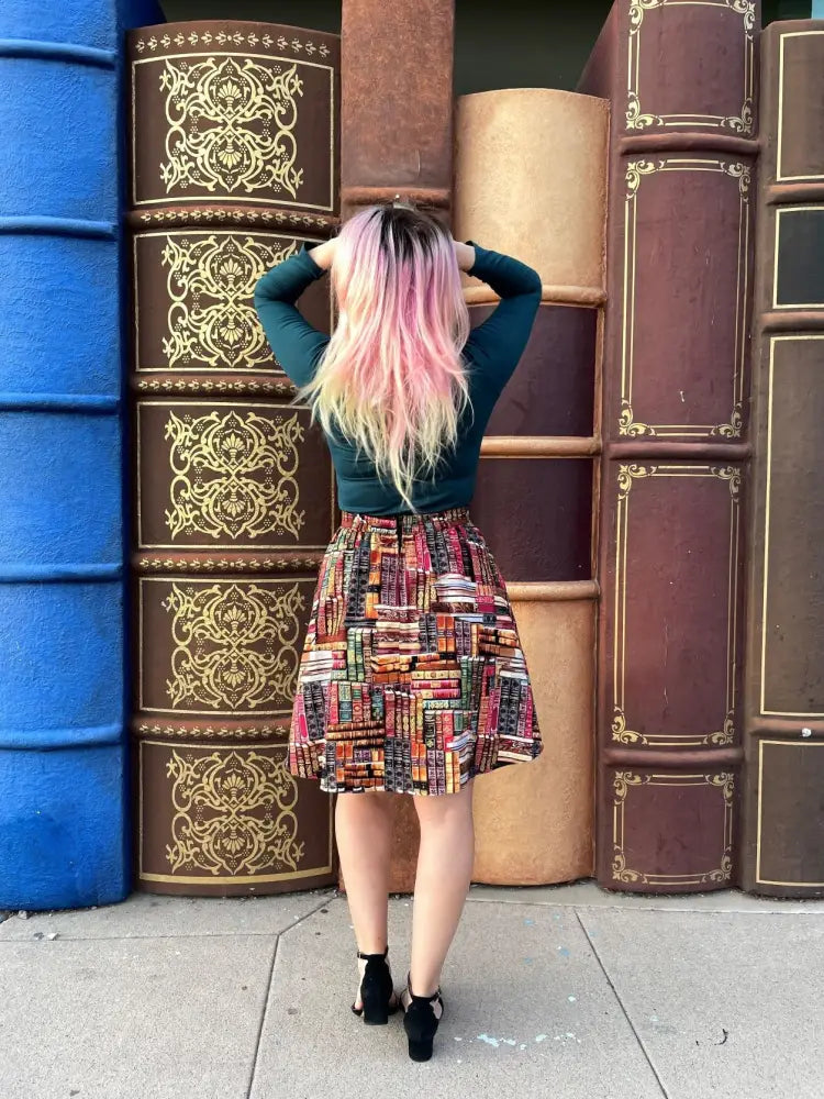 A woman wearing a hunter green vintage stretch mock neck top with a colorful patchwork skirt featuring bookshelf patterns