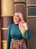 A woman wearing a hunter green vintage stretch mock neck top with long sleeves and a colorful book-themed skirt