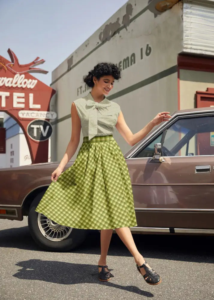 A woman wears a green plaid Doris cotton A-line skirt with pockets paired with a sleeveless light green blouse