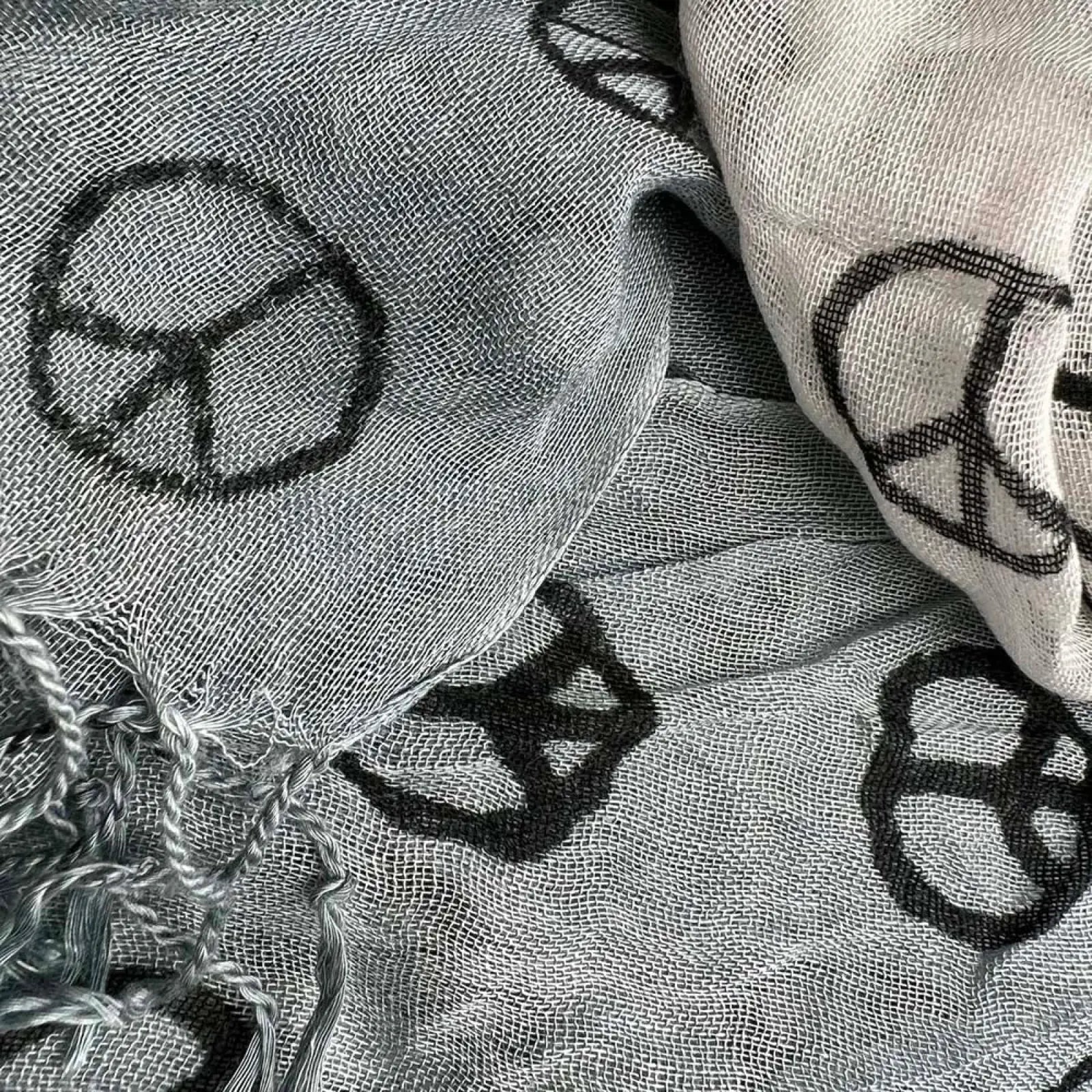 A light gray viscose scarf featuring black peace symbols with a loosely woven texture and frayed edges