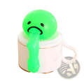 A bright green squishy Gudetama vomiting egg yolk stress relief toy with a sad face sits on a white ceramic mug