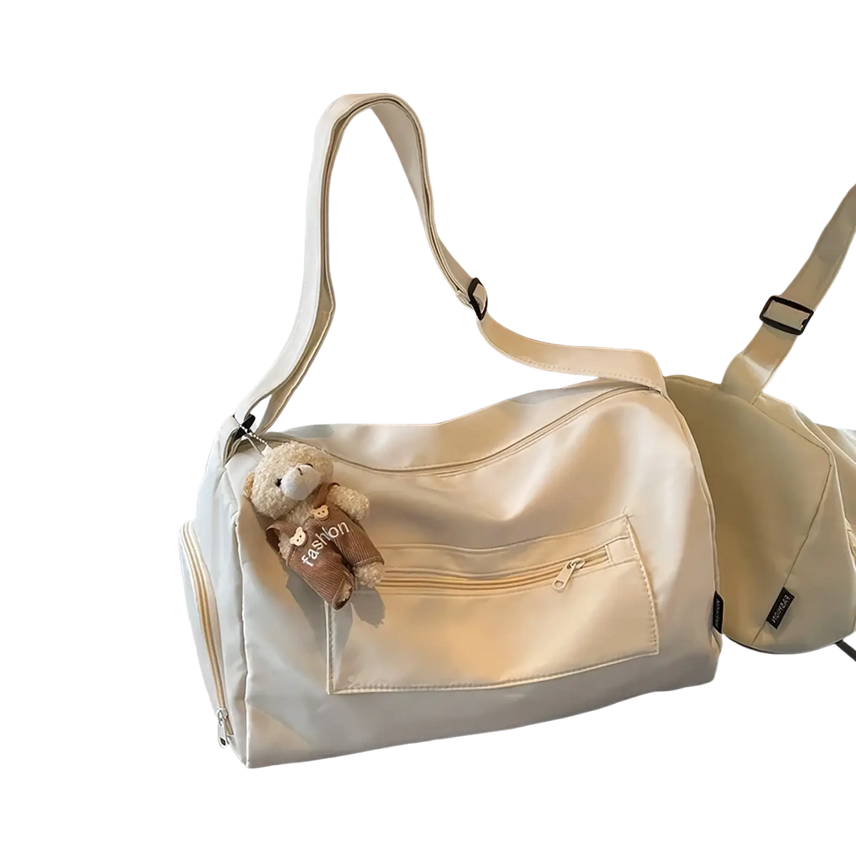 Cream-colored nylon gym duffle bag with detachable shoulder strap and front zippered pocket featuring teddy bear charm