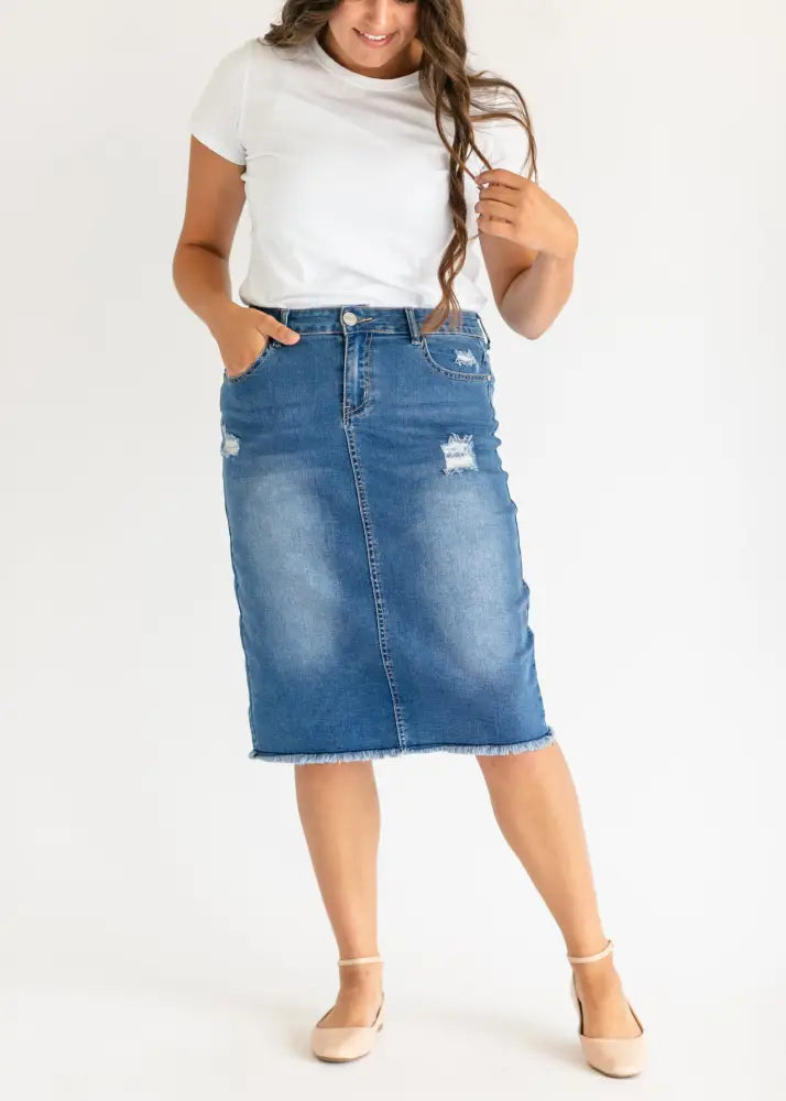 Hadley high rise distressed denim midi skirt in blue with mid-thigh length, distressed patches, and frayed hem