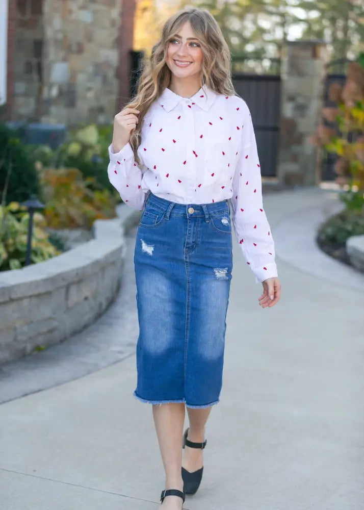 White blouse with red heart patterns and long sleeves paired with hadley high rise distressed denim midi skirt