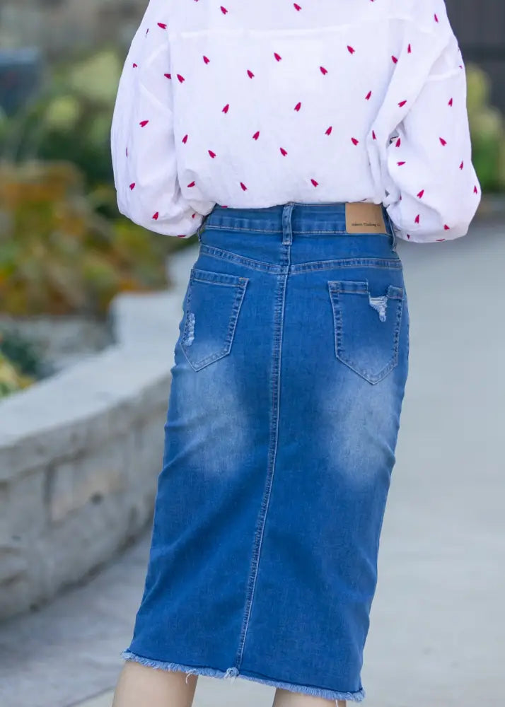 Blue denim hadley high rise midi skirt with frayed hem and distressed back pockets shown from the back side