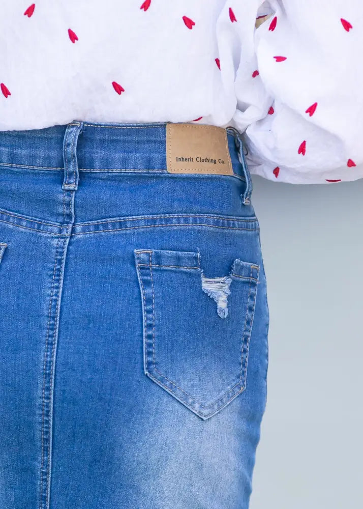 Back side of a blue denim hadley high rise distressed midi skirt with a tan leather inherit clothing co brand patch