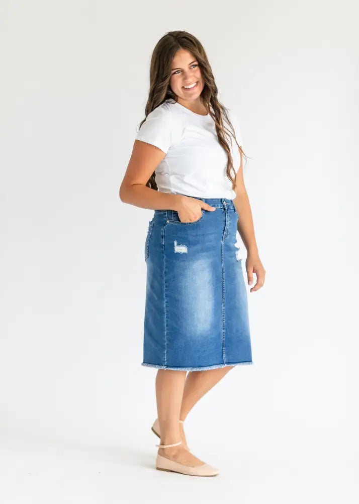 Hadley high rise distressed denim midi skirt in faded blue with mid-thigh length, frayed hem, and side patches