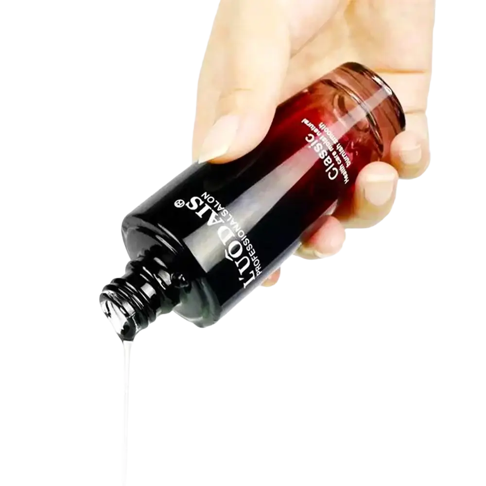 A sleek dark amber 80ml hair essential oil bottle by tudas for hair loss and frizzy hair is held with liquid dripping