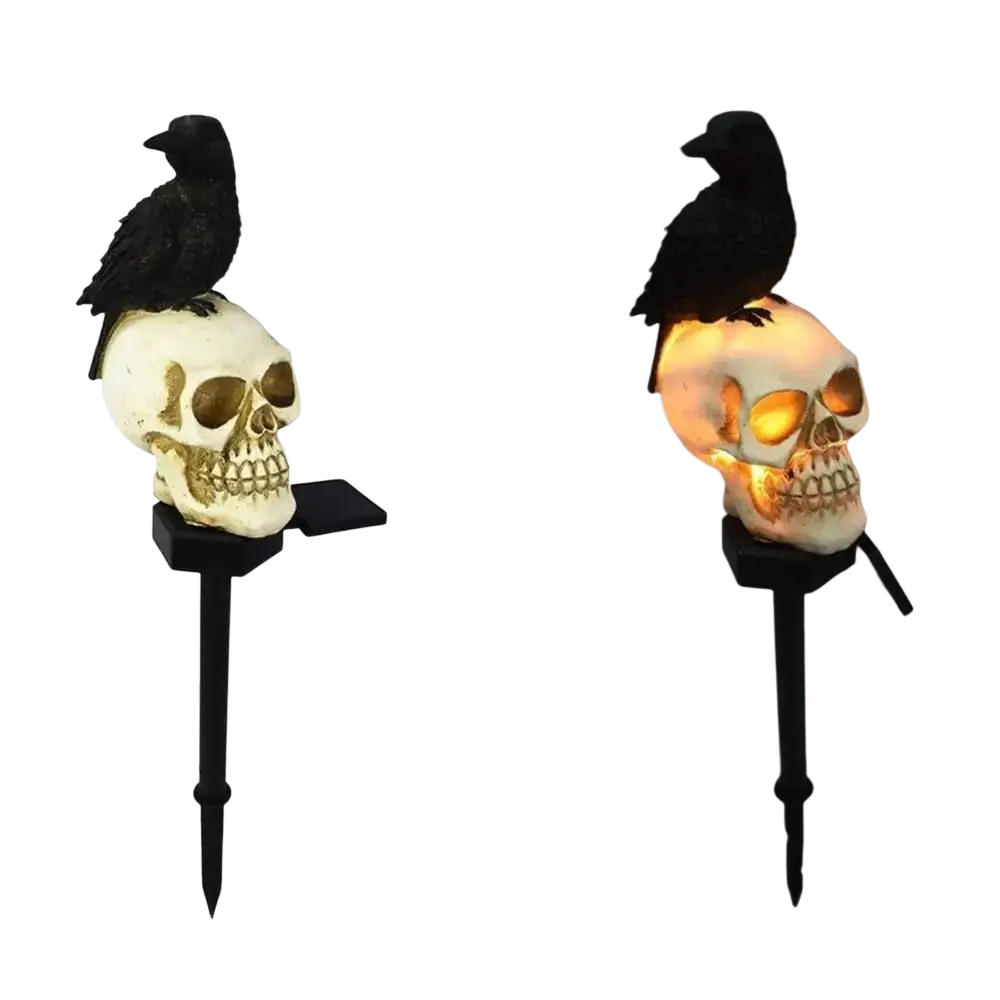 Black crow perched on a white skull with gold eye sockets illuminated by warm light halloween outdoor light skeleton stake