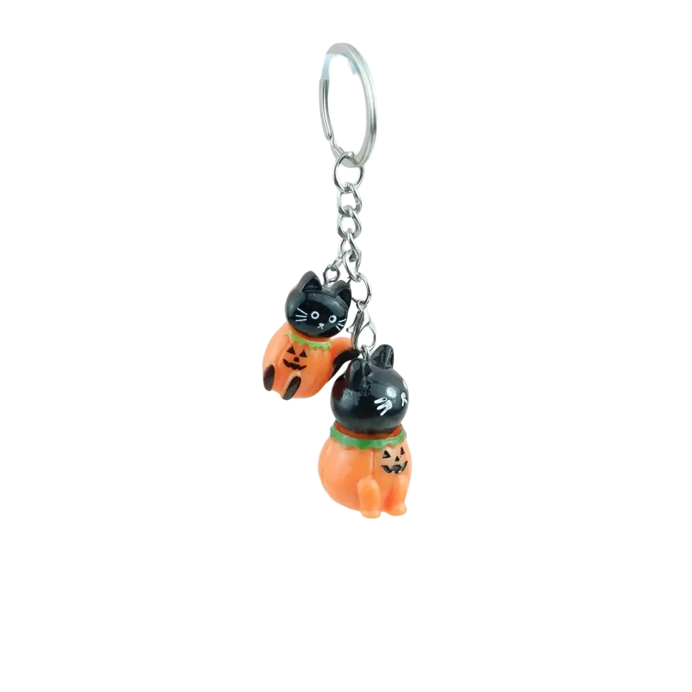 A handmade resin halloween pumpkin keychain with two black cat figurines in orange costumes on a silver ring