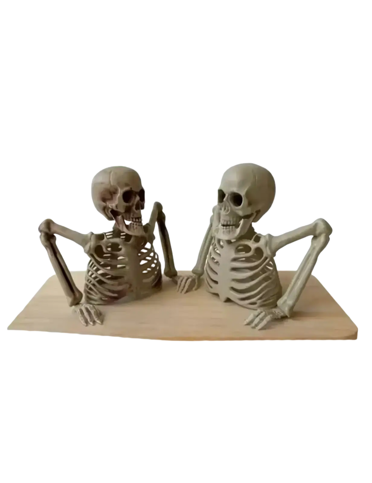 Two beige plastic skeleton props seated side by side on a light wooden surface for creepy indoor outdoor decor
