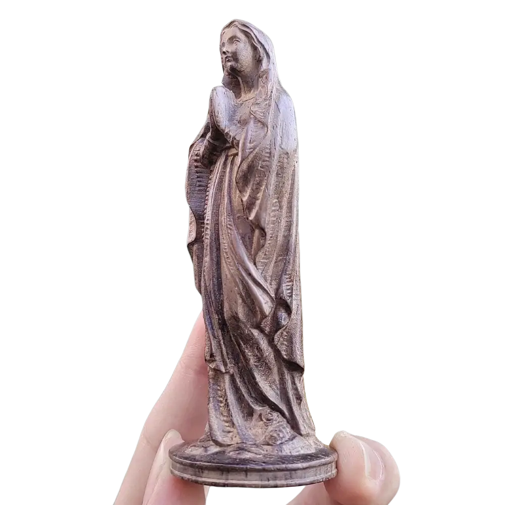 Hand carved wooden virgin mary figurine with bronze color detailed robes held against blurred green foliage background