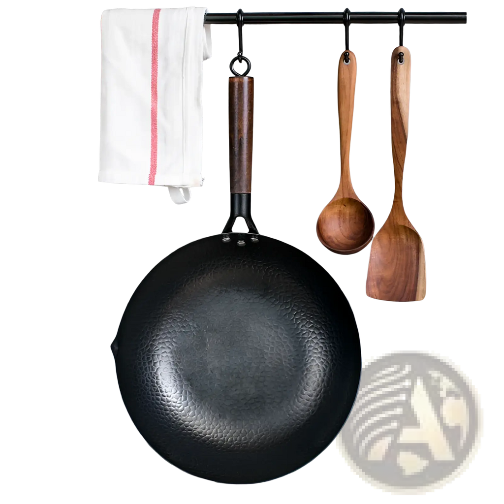 Handmade black hammered steel wok with dark wooden handle hanging on rack with glass lid nearby
