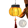 A handmade persimmon paper lantern glowing yellow with intricate orange and blue floral patterns and butterfly top