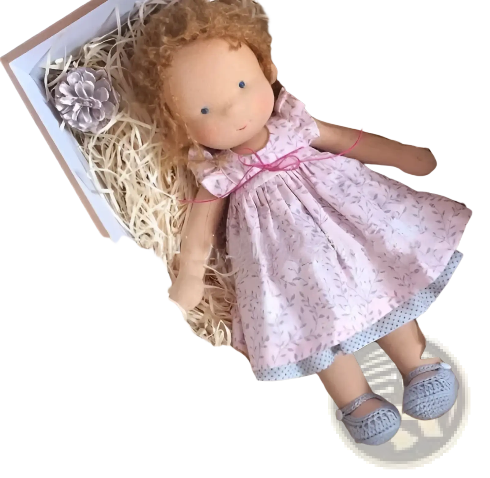 Handmade plush doll with golden curly auburn hair and blue eyes wearing a pink floral dress and gray crocheted shoes