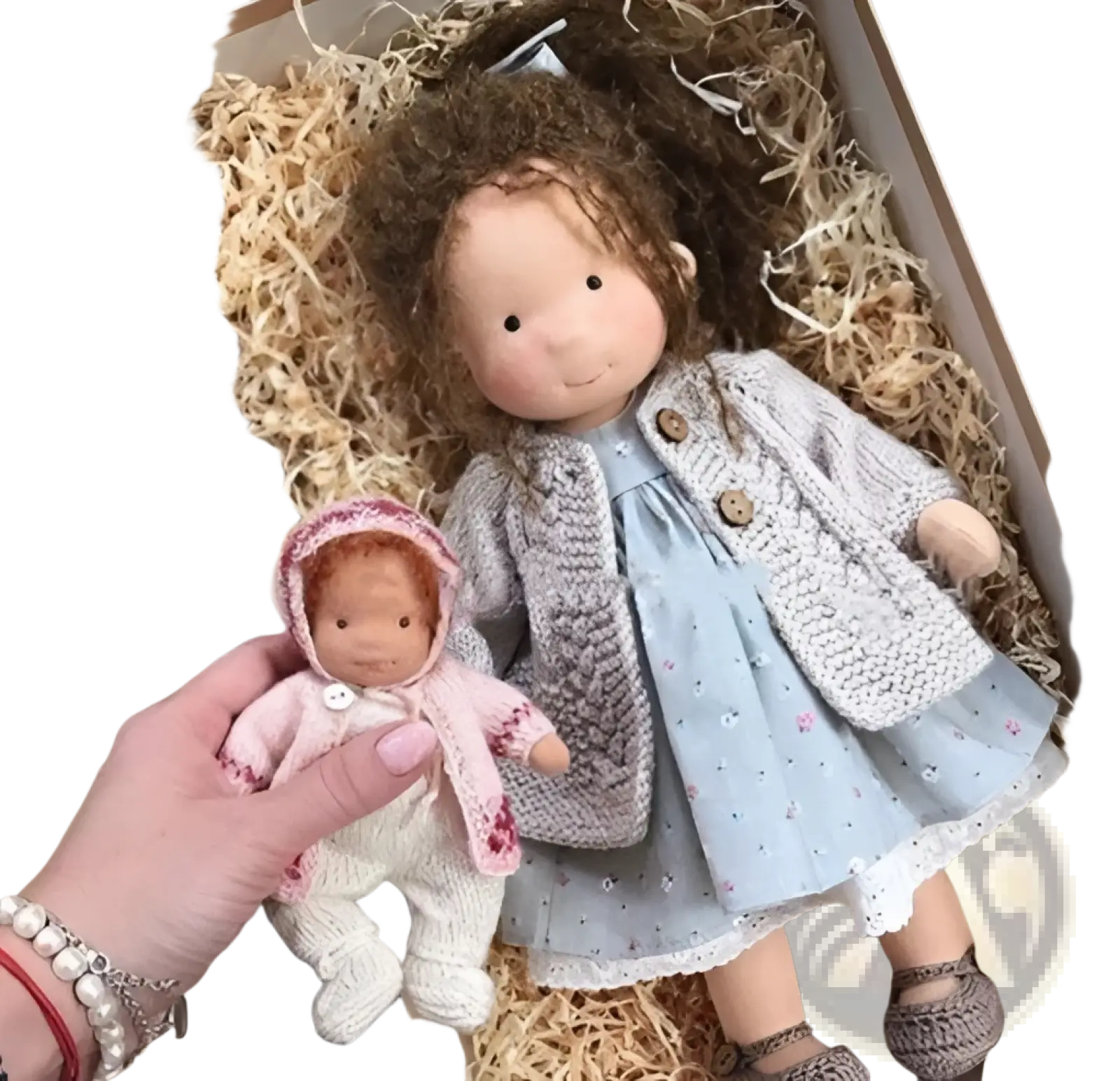 A hand holds a handmade plush doll with golden curly hair dressed in a pink knitted hooded outfit and mittens