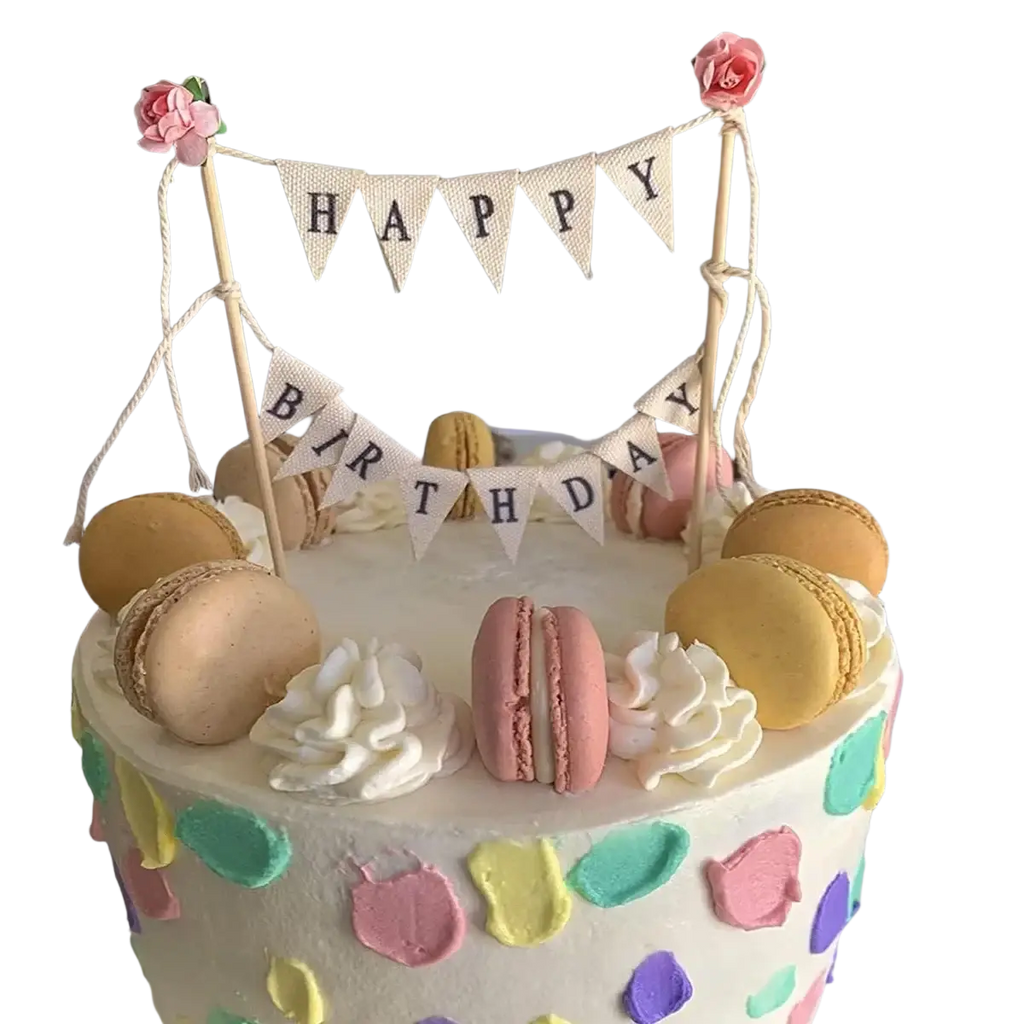 A pastel happy birthday cake with colorful macarons white frosting swirls and a bunting topper with pink roses