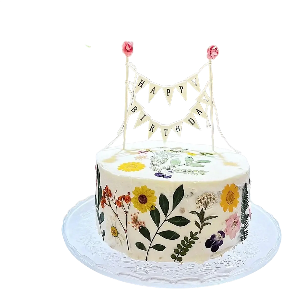 A white birthday cake with a happy birthday cake bunting topper and pressed yellow pink and purple flowers