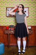 Woman wearing harper black satin pleated skater skirt with pockets paired with black and white houndstooth top