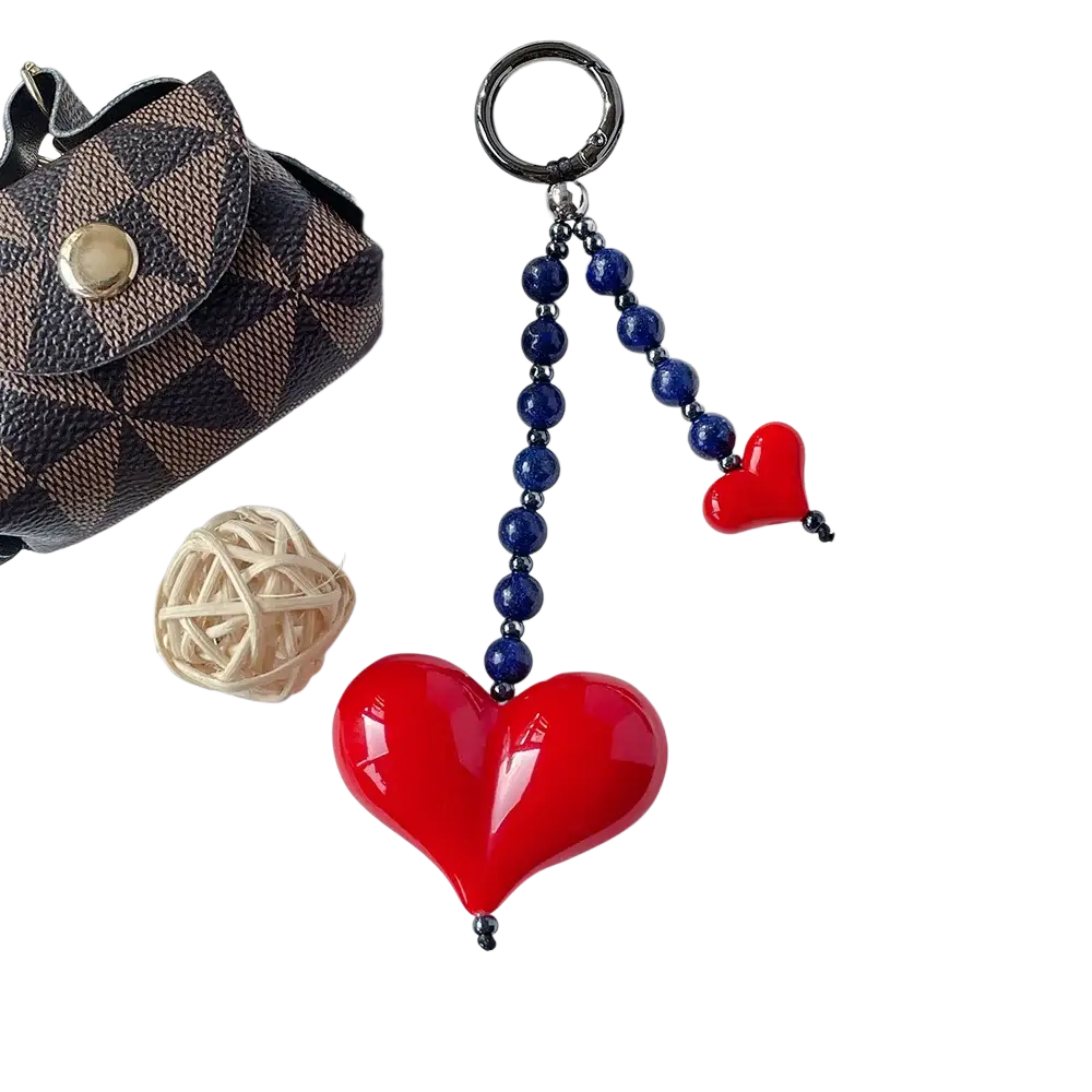 A glossy red heart keychain with dark blue beaded chain and silver ring for use as a bag charm