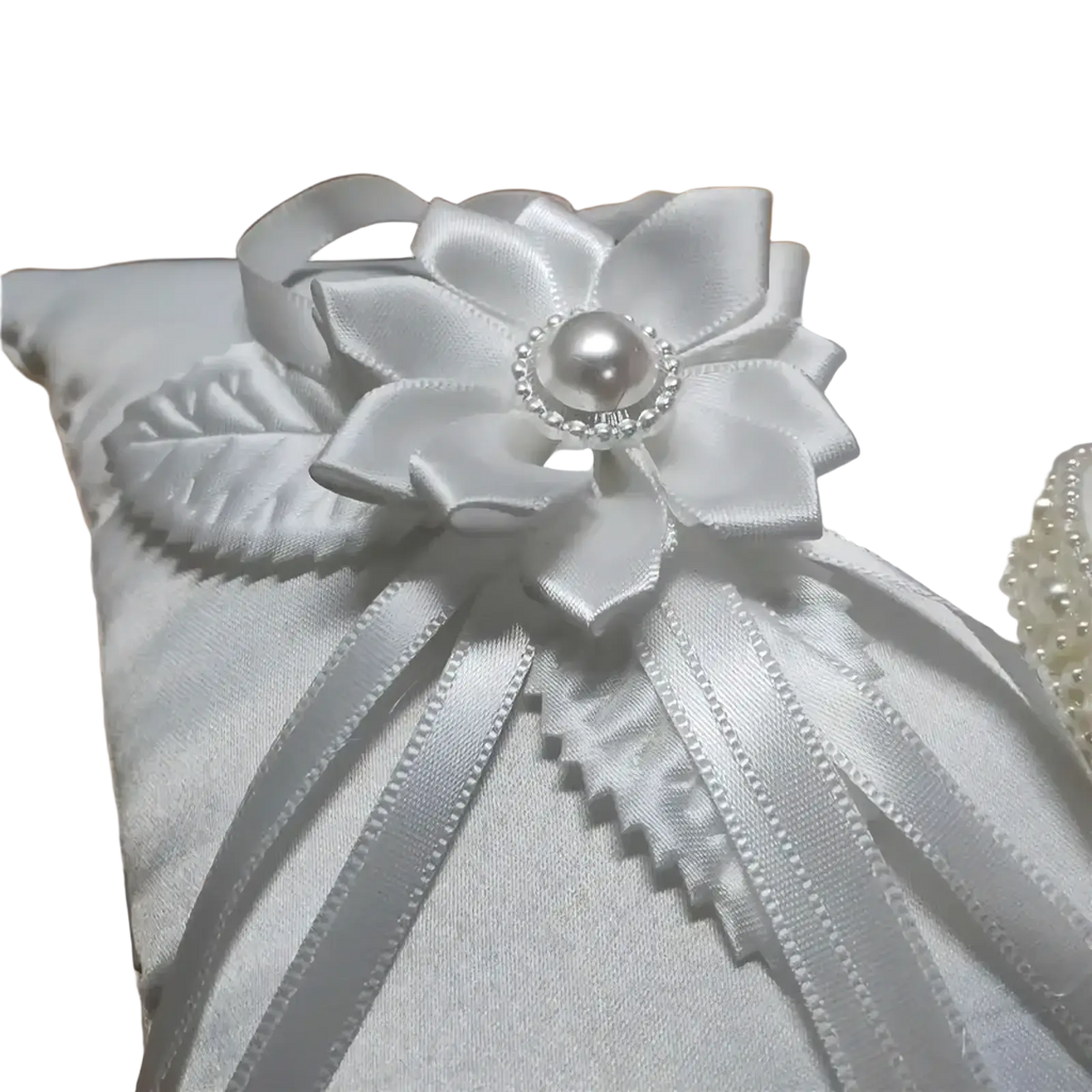 Heart wedding ring pillow in white satin featuring a large ribbon flower with pearl and rhinestone accents for ceremony
