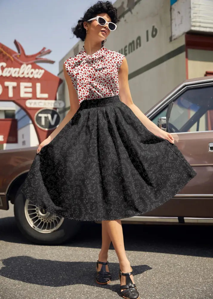 A black full skirted dress with a subtle pattern and fitted bodice paired with vintage 1950s white sleeveless heart print bow top
