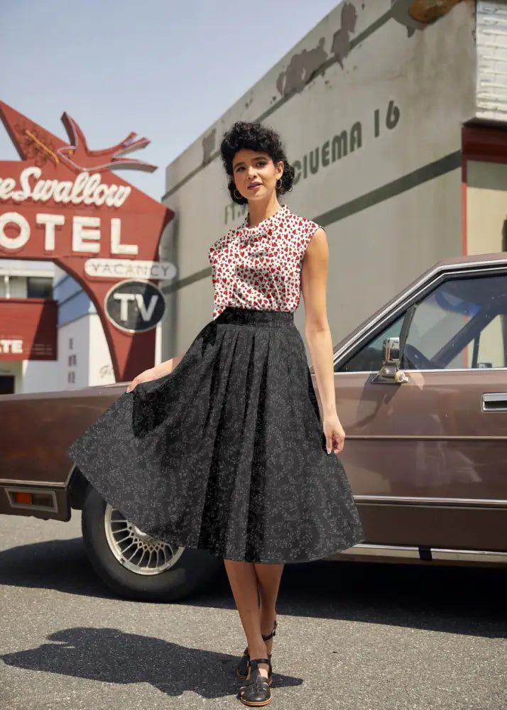 A black patterned high waist a-line skirt with a flared hem paired with a vintage 1950s white sleeveless heart print bow top
