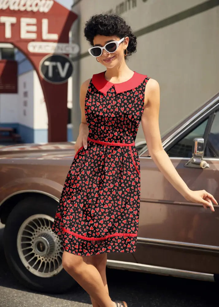 A sleeveless black cotton dress with red peter pan collar trim and small red heart pattern called retro hearts
